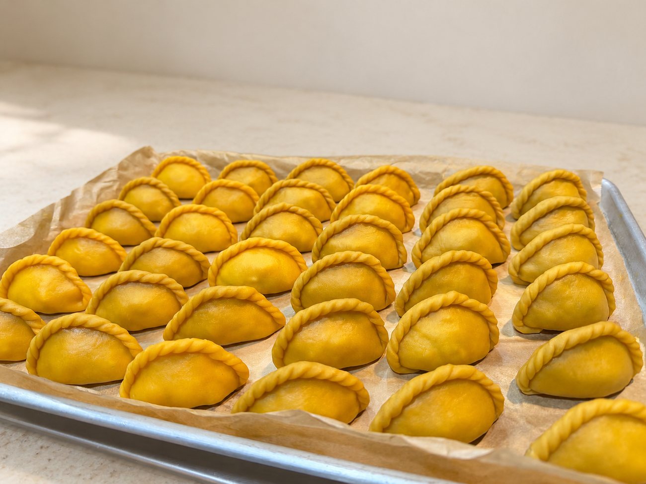 A tray of unbaked salteñas, golden dough with braided seams